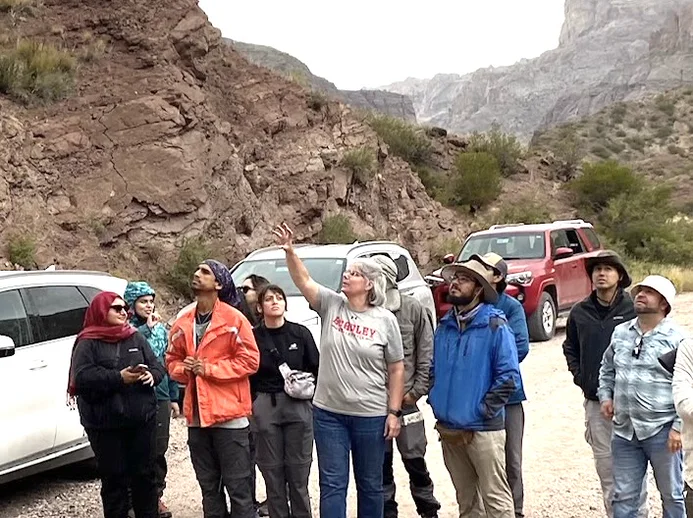 A field-trip leader pointing out a rock face to a group in a desert canyon