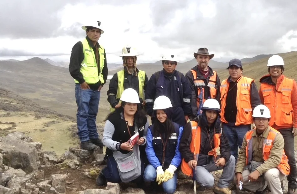 A field-trip group in hard hats and safety vests on a rocky highland outcrop